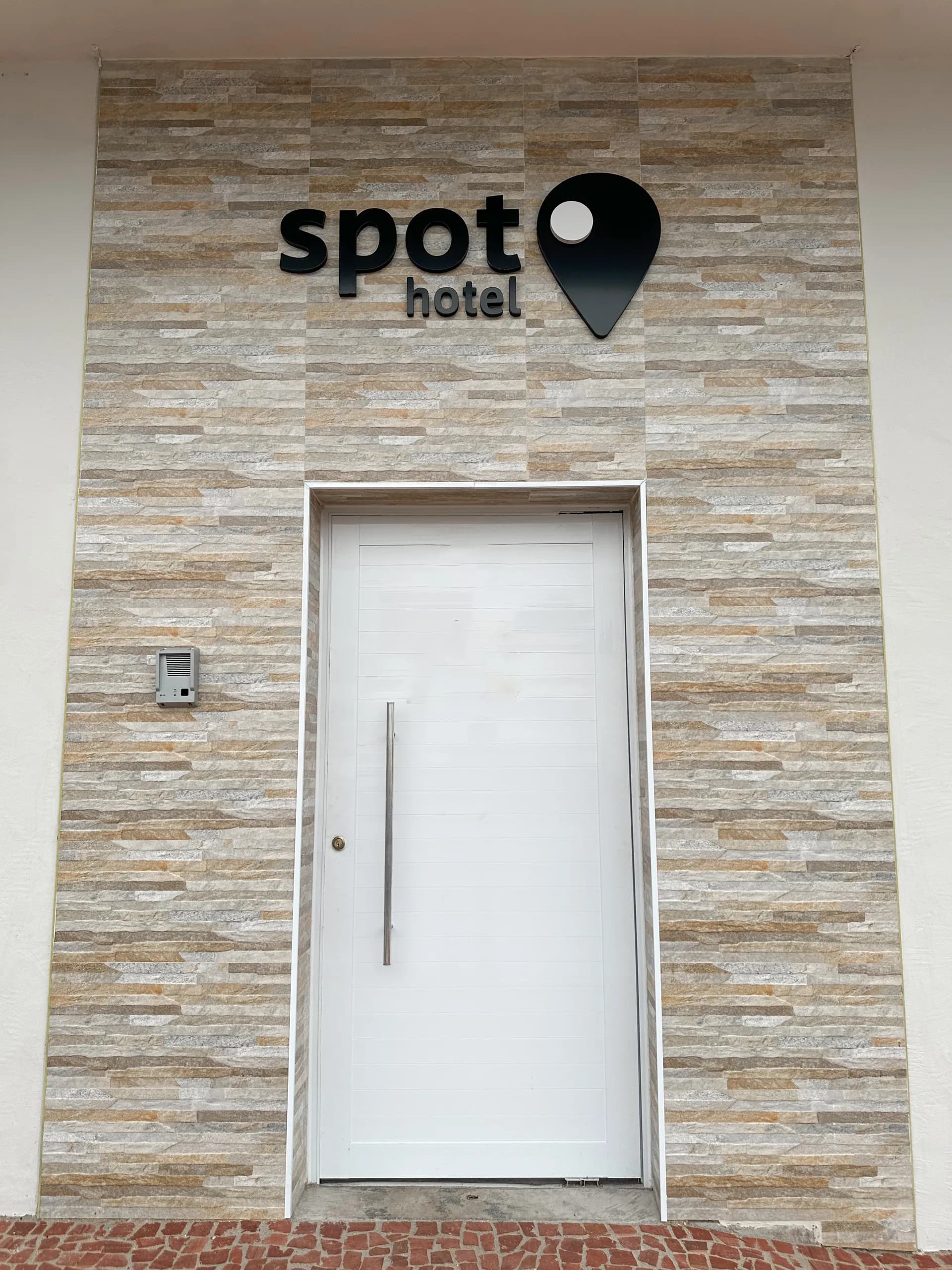 Porta de entrada do Spot Hotel com a logo na parede revestida de pedra