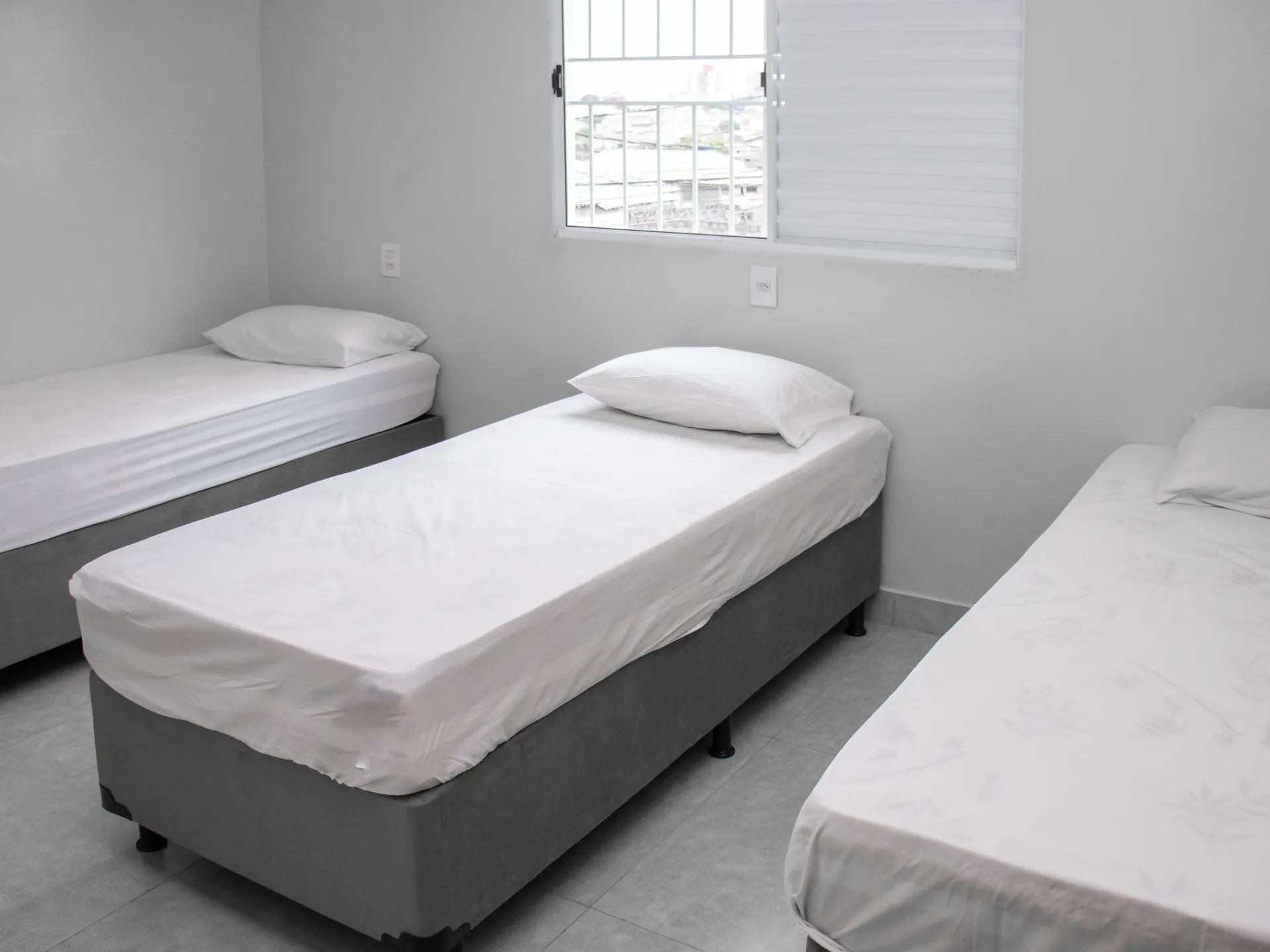 Quarto com três camas de solteiro e janela
